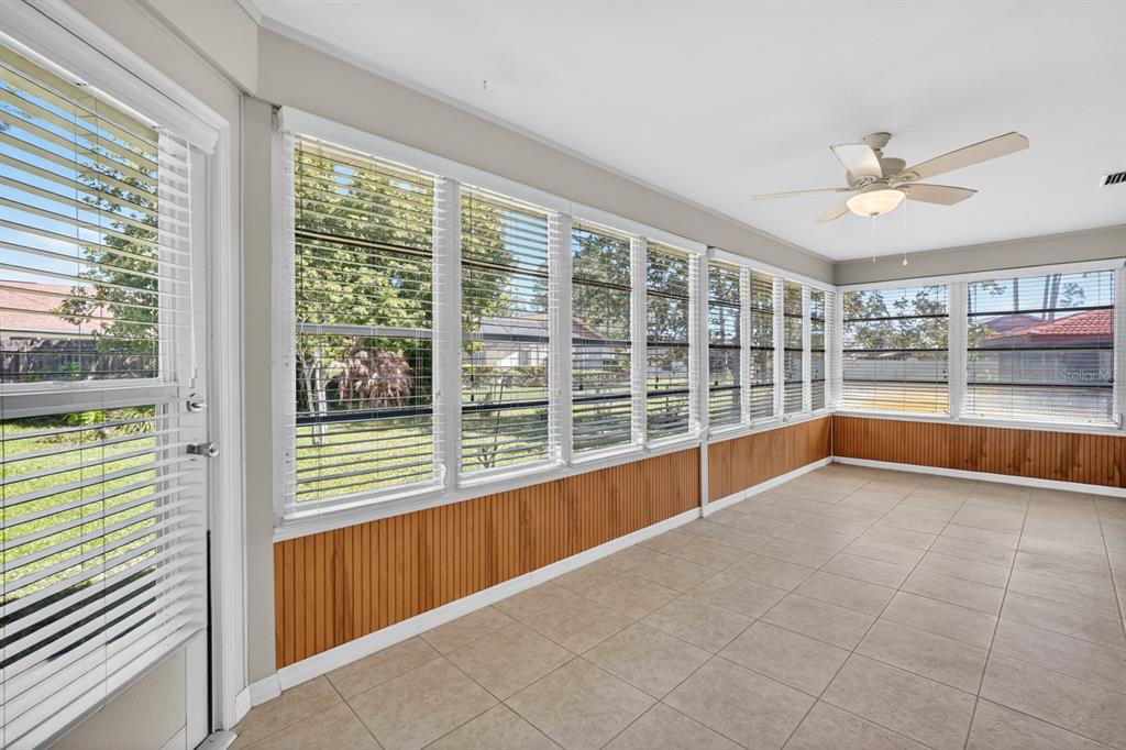 A sunroom with tile flooring, wood paneling, large windows with blinds, and a ceiling fan — 153 WELLSTONE DRIVE, PALM COAST, FL