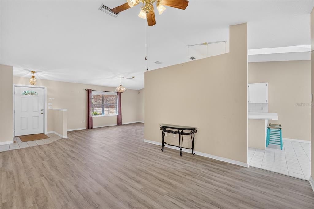 An open living area features light wood-look flooring, a ceiling fan, and a kitchen entrance — 153 WELLSTONE DRIVE, PALM COAST, FL