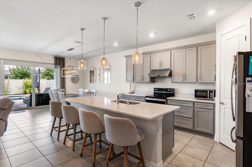 A kitchen with a large island, gray cabinetry, and pendant lighting overlooking a backyard pool — 2712 TIMBERGROVE STREET, ST CLOUD, FL