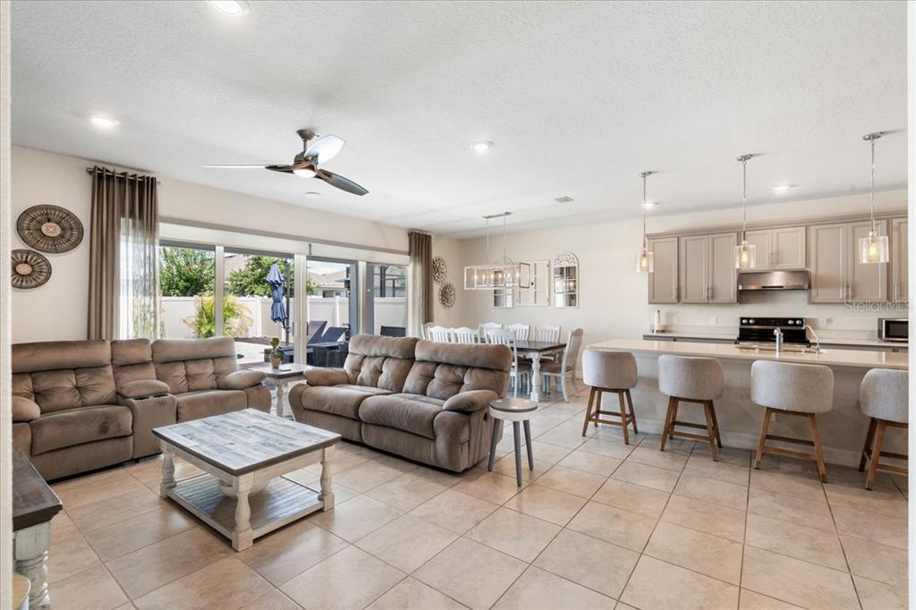 An open-concept living room and kitchen featuring tile flooring, neutral cabinetry, and sliding glass doors — 2712 TIMBERGROVE STREET, ST CLOUD, FL