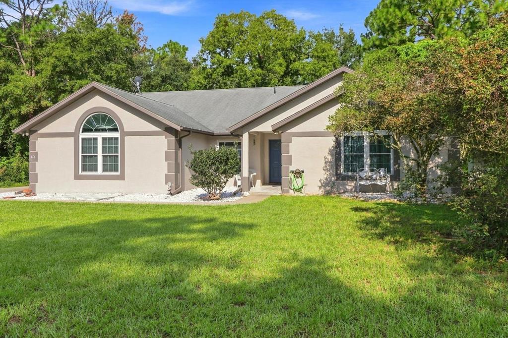 A single-story house with a beige stucco exterior, dark trim, and a front lawn — 11 LIDFLOWER COURT, HOMOSASSA, FL