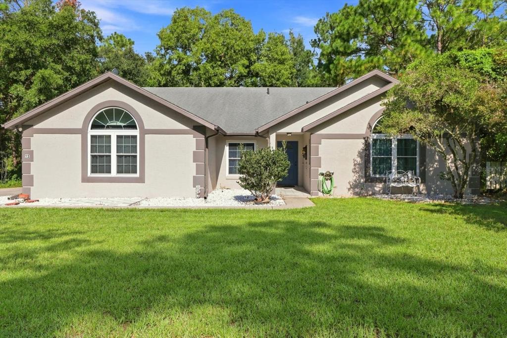 A single-story house with a light-colored stucco exterior, dark trim, and a front lawn — 11 LIDFLOWER COURT, HOMOSASSA, FL