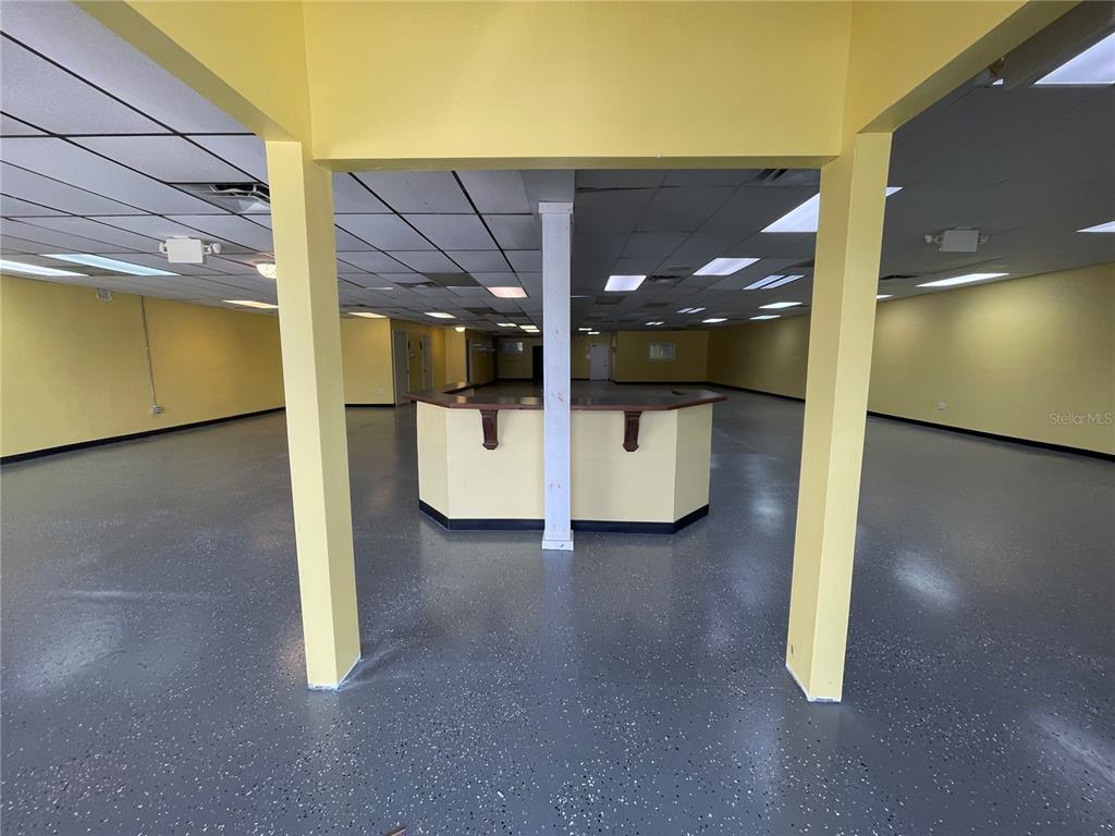 A large, empty commercial space features yellow walls, a drop ceiling, and a central counter — 7127 US HIGHWAY 19, NEW PORT RICHEY, FL