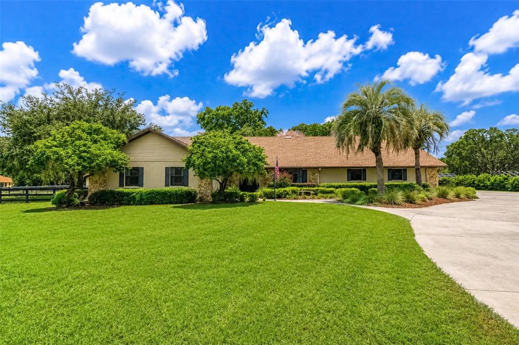 A single-story house with a tan exterior, stone accents, and palm trees sits behind a lawn — 6899 SW 99TH STREET, OCALA, FL