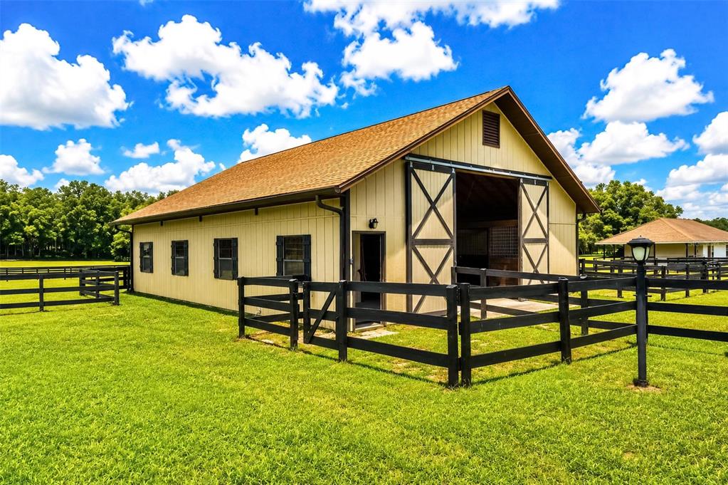A tan barn with black trim and sliding doors sits in a grassy fenced pasture — 6899 SW 99TH STREET, OCALA, FL