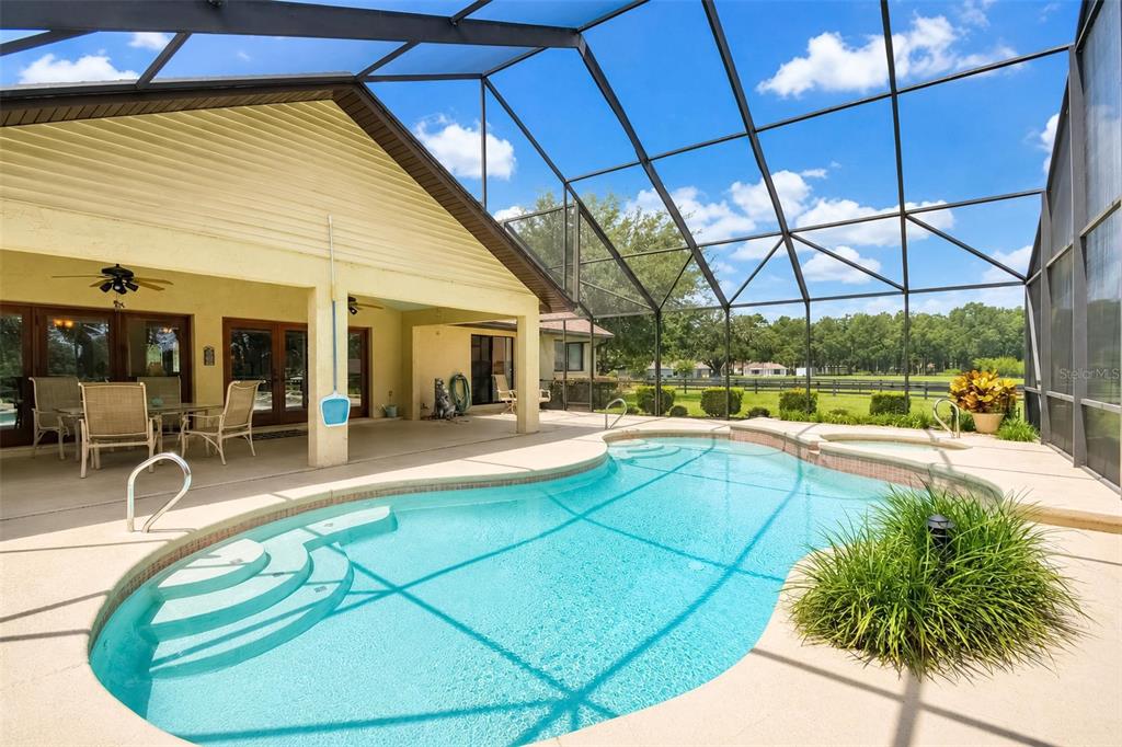 A swimming pool and hot tub are enclosed within a screened-in patio behind a house — 6899 SW 99TH STREET, OCALA, FL