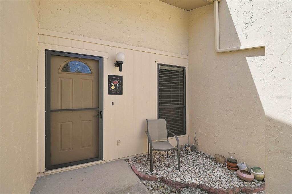 An exterior view of a home entrance with a screen door, window, and gravel patio — 3189 GLEN ELYN BOULEVARD UNIT 3, SARASOTA, FL