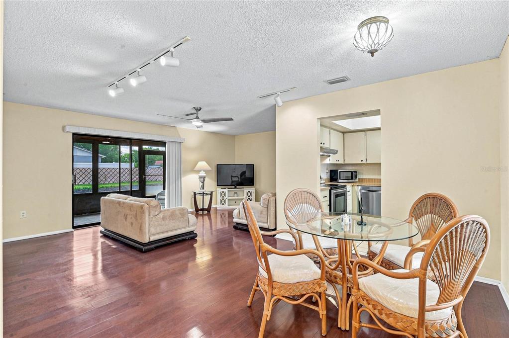 An open-concept living and dining area features hardwood floors, a glass-top table, and sliding doors — 3189 GLEN ELYN BOULEVARD UNIT 3, SARASOTA, FL