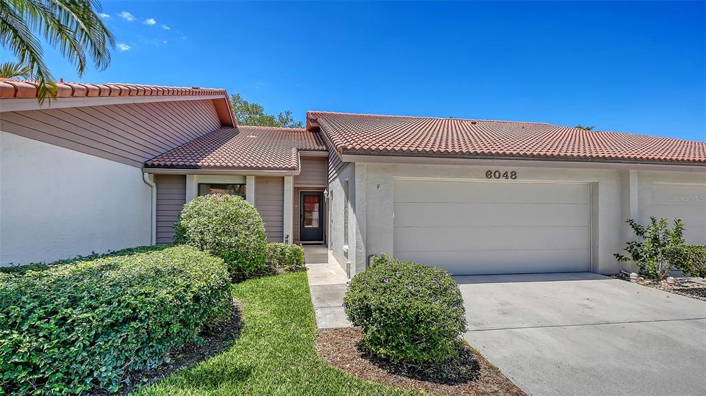 A single-story house features a two-car garage, a tiled roof, and a front entryway — 6048 WILSHIRE BOULEVARD UNIT 2, SARASOTA, FL