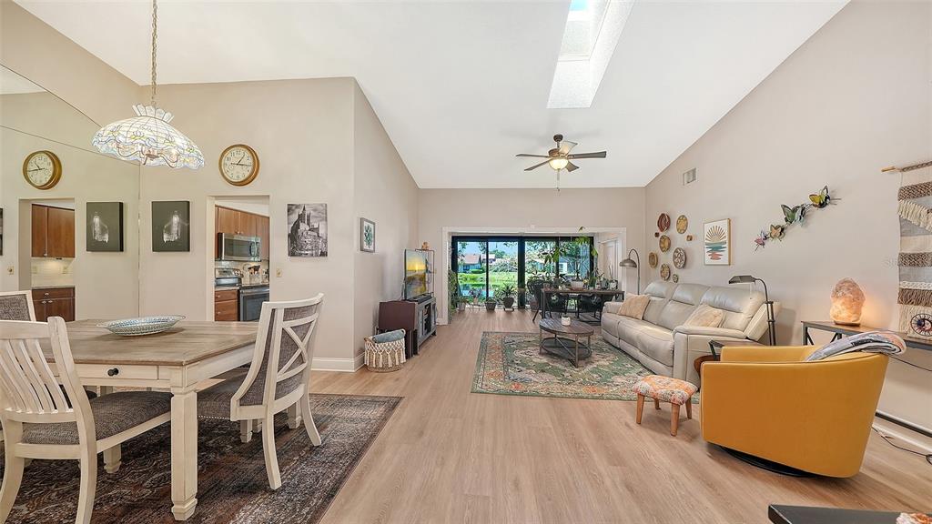 An open-concept living and dining area with light wood flooring, vaulted ceilings, and a patio — 6048 WILSHIRE BOULEVARD UNIT 2, SARASOTA, FL