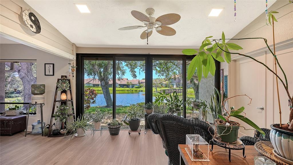 A sunroom with wood-look flooring, a ceiling fan, and large windows overlooking a pond — 6048 WILSHIRE BOULEVARD UNIT 2, SARASOTA, FL