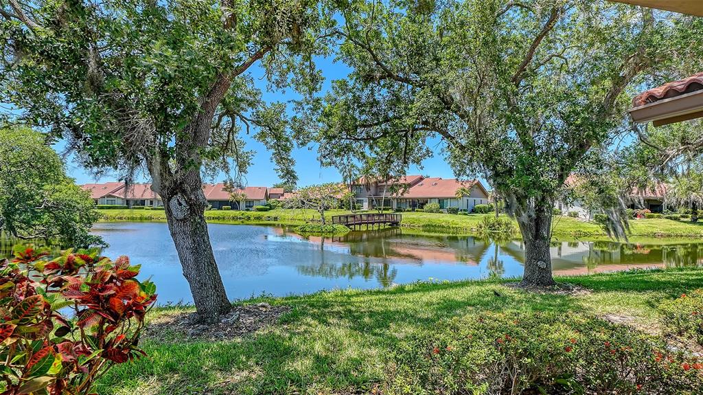 A view of a pond with a wooden footbridge surrounded by trees and residential buildings — 6048 WILSHIRE BOULEVARD UNIT 2, SARASOTA, FL