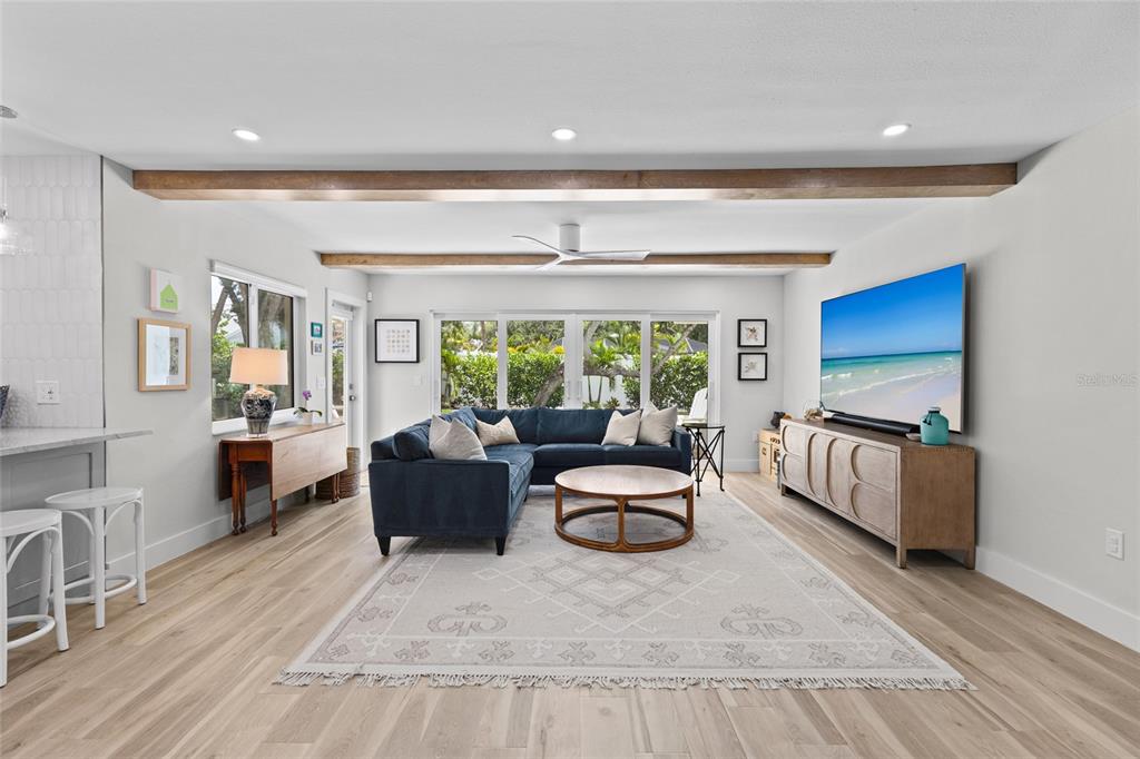 A living room features a blue sectional sofa, wood beams, and light wood flooring — 801 EDGEMERE LANE, SARASOTA, FL