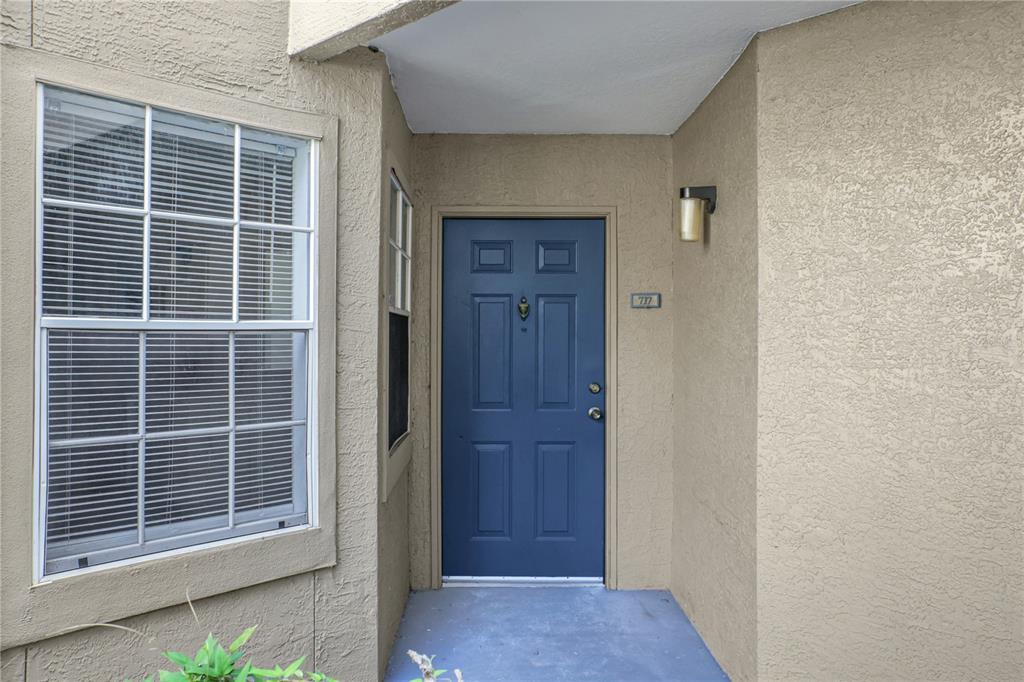 A blue front door with a brass knocker is set into a beige stucco exterior wall — 7300 WESTPOINTE BOULEVARD UNIT 717, ORLANDO, FL
