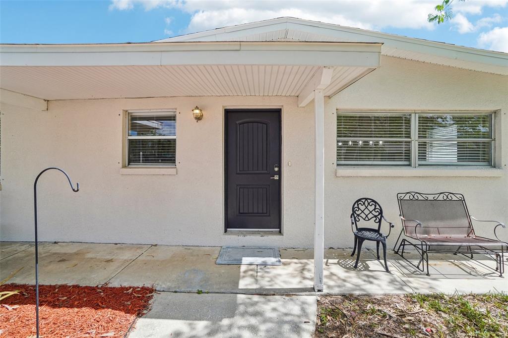 A covered concrete porch features a dark front door, two windows, and outdoor seating — 541 FIREFLY LANE, APOLLO BEACH, FL