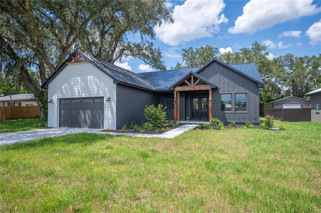 A modern single-story house with dark gray board-and-batten siding, a metal roof, and wood accents — 2411 OLD MEDULLA ROAD, LAKELAND, FL