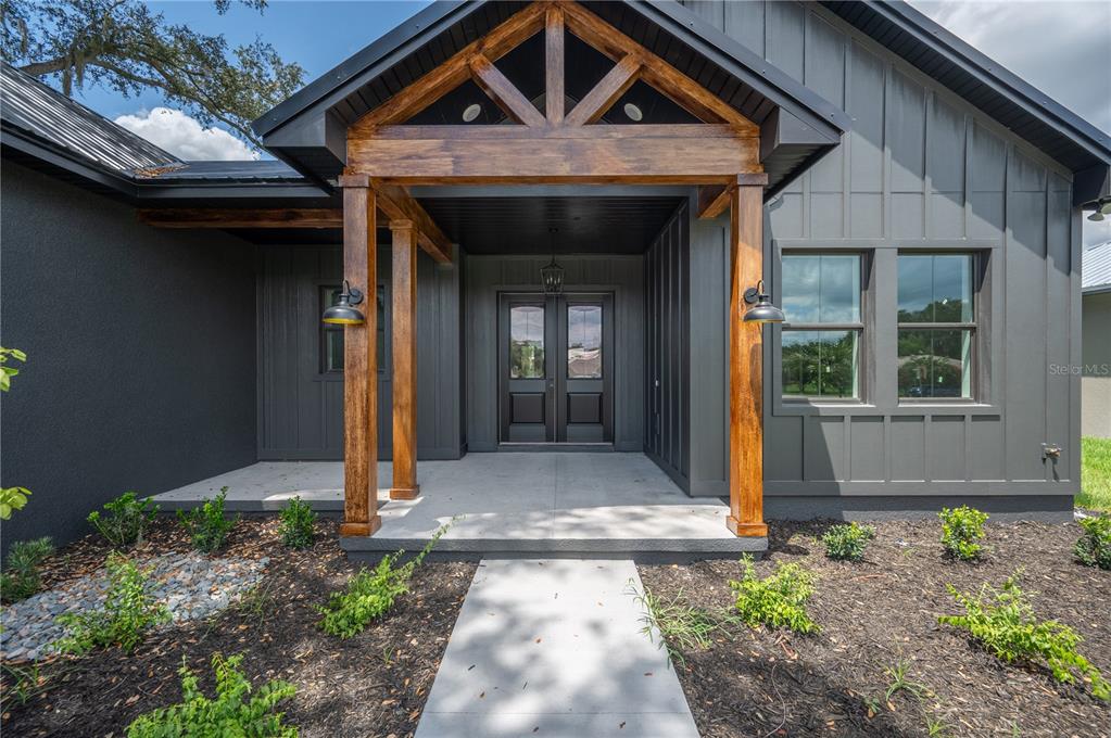 A modern dark gray house exterior features a wooden porch gable and double front doors — 2411 OLD MEDULLA ROAD, LAKELAND, FL