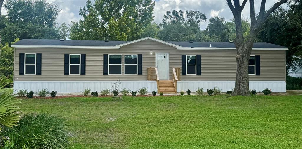 A single-story manufactured home with tan siding, black shutters, and a wooden front porch — 5135 TURTLE DOVE TRAIL, LAKELAND, FL