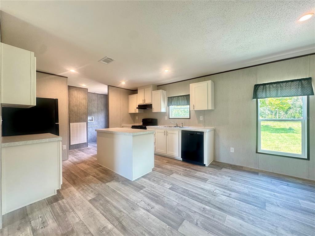 A kitchen with white cabinets, a central island, black appliances, and wood-look flooring — 5135 TURTLE DOVE TRAIL, LAKELAND, FL