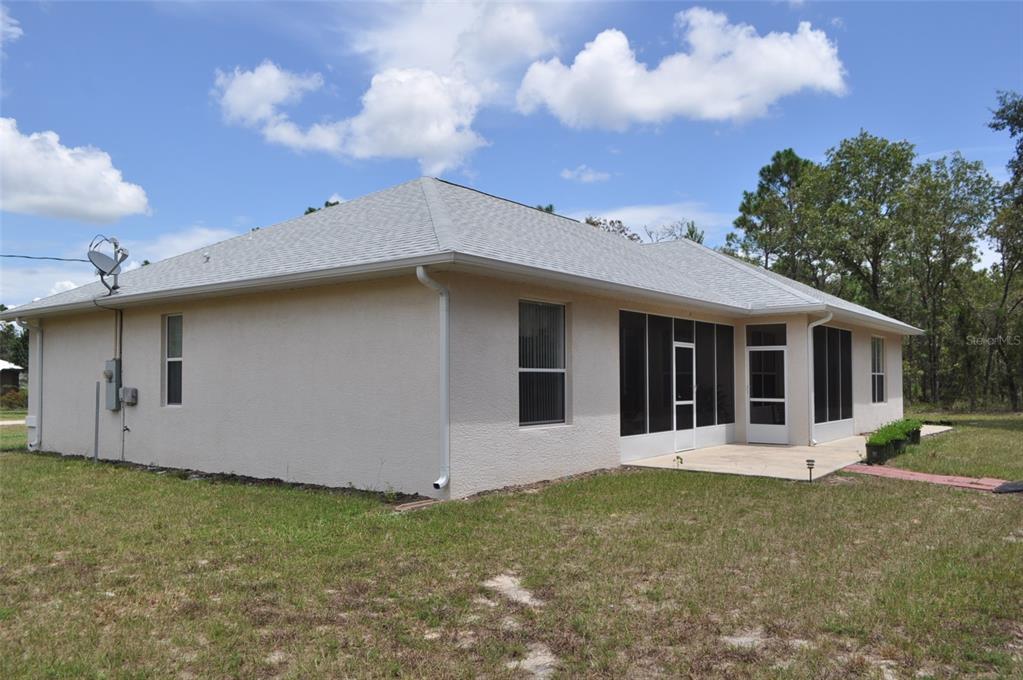 The exterior of a beige stucco house features a screened-in back porch and a shingled roof — 15580 NE 16TH LANE, WILLISTON, FL