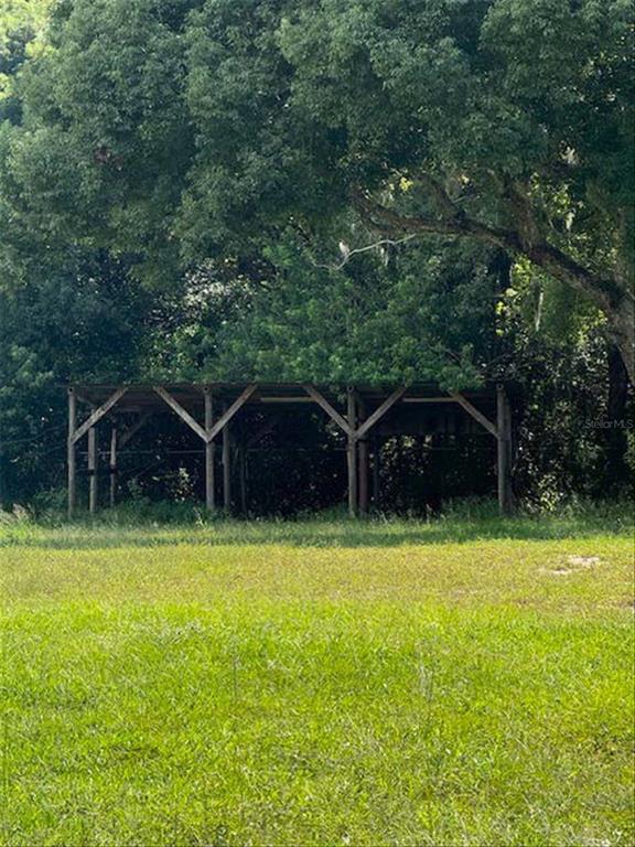 A wooden open-sided shed stands in a grassy field in front of a dense tree line — 1015 E 10TH STREET, ST CLOUD, FL
