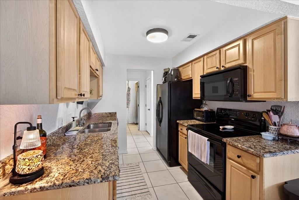 A galley kitchen features light wood cabinets, granite countertops, black appliances, and white tile flooring — 12 BRIGANTINE CT COURT, ST AUGUSTINE, FL