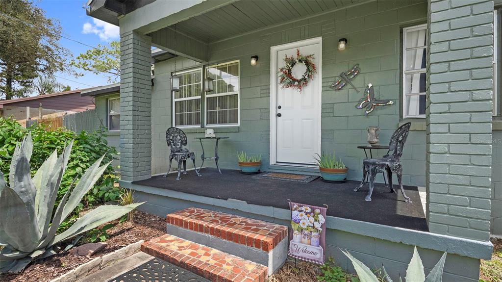A covered front porch with a brick-stepped entrance, green painted block walls, and patio furniture — 8709 EL PORTAL DRIVE, TAMPA, FL