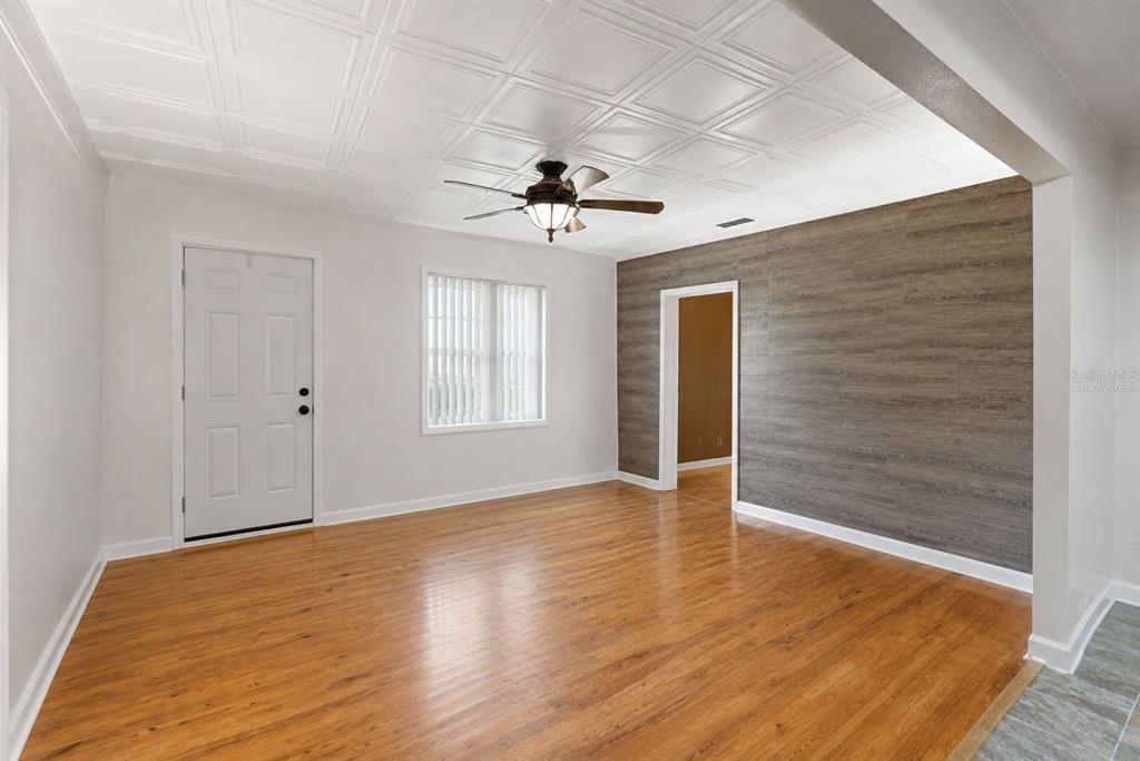 An empty room features wood-look flooring, a coffered ceiling, and an accent wall with wood planks — 8709 EL PORTAL DRIVE, TAMPA, FL