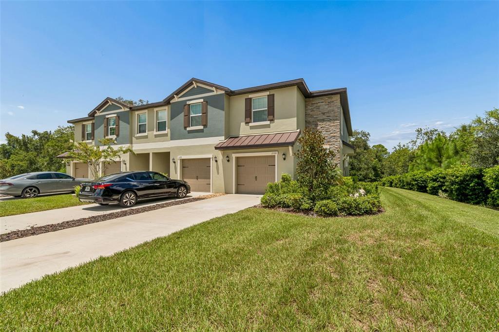 A two-story townhouse with a stone-accented exterior, two garages, and a concrete driveway — 11166 WISHING CLOUD ROAD, LAND O LAKES, FL