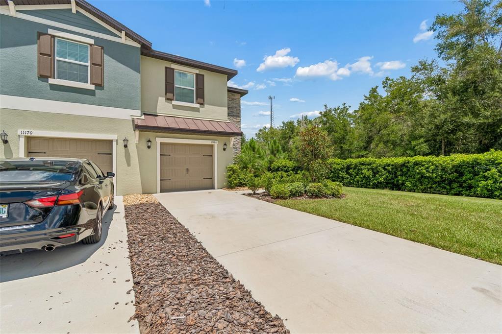 A two-story townhouse exterior features a concrete driveway, a black car, and a grassy yard — 11166 WISHING CLOUD ROAD, LAND O LAKES, FL