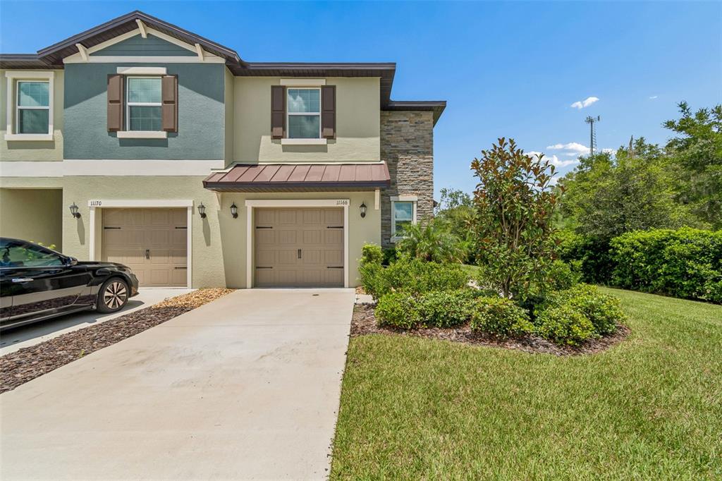 A two-story townhouse exterior features tan stucco, a stone accent wall, and two garage doors — 11166 WISHING CLOUD ROAD, LAND O LAKES, FL