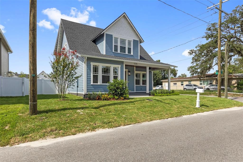A two-story blue house with a front porch and a white fence on a lawn — 1224 E CHELSEA STREET, TAMPA, FL