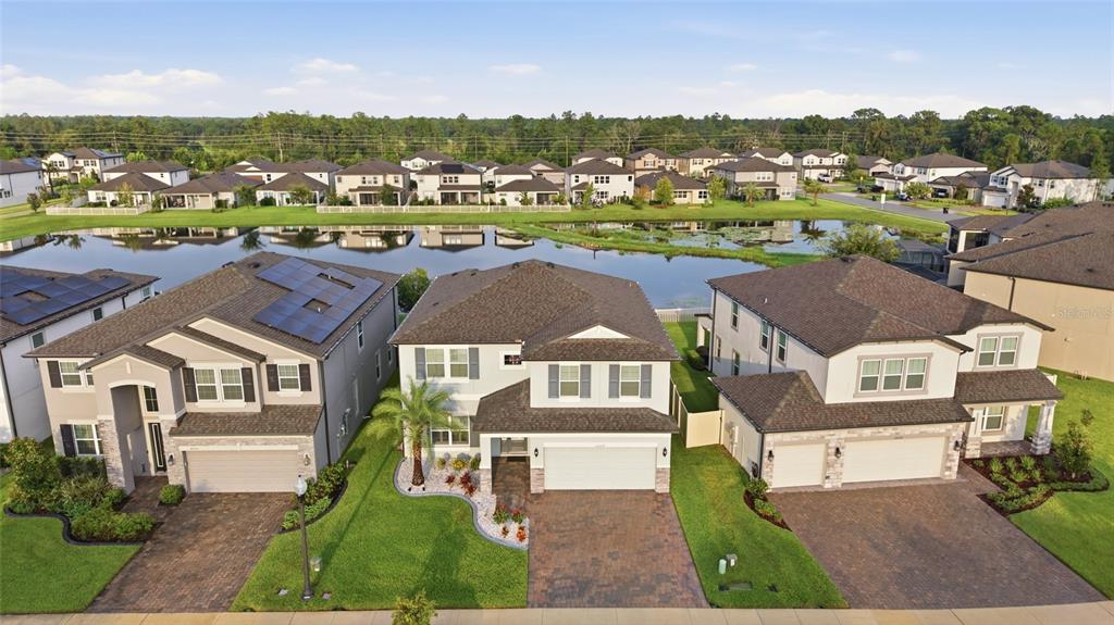 An aerial view shows three suburban houses with paved driveways facing a small pond — 22319 WOODMEN HALL DRIVE, LAND O LAKES, FL