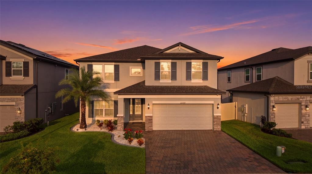 A two-story suburban house with a paved driveway, a palm tree, and a sunset sky — 22319 WOODMEN HALL DRIVE, LAND O LAKES, FL