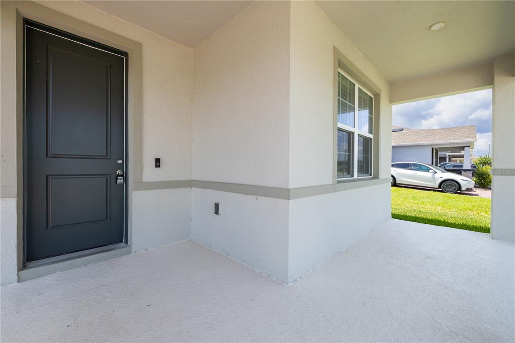 A covered front porch features a dark gray door and a window on a stucco wall — 3754 ISLE ROYAL PLACE, APOPKA, FL