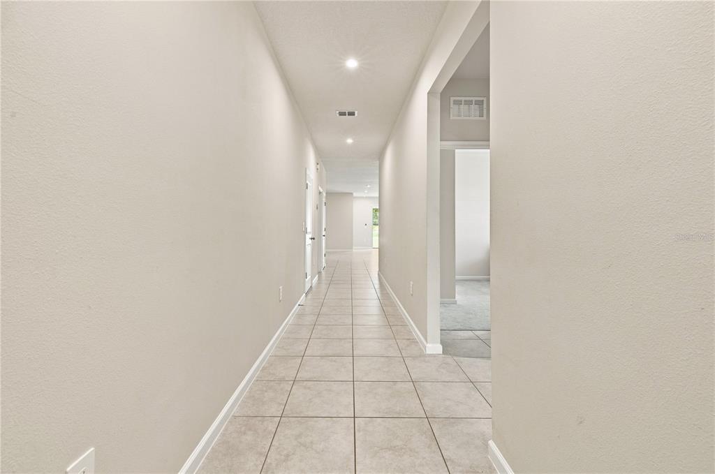 A long hallway with light-colored tile flooring and neutral walls leads toward a bright doorway — 3754 ISLE ROYAL PLACE, APOPKA, FL