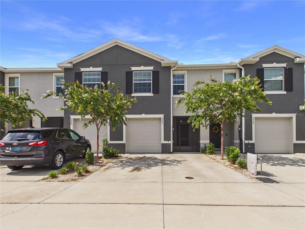 A row of two-story townhomes with gray stucco facades, attached garages, and concrete driveways — 5262 DRAGONFLY DRIVE, WILDWOOD, FL