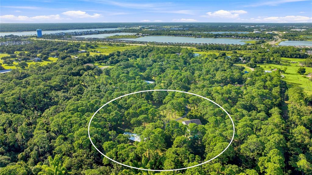 An aerial view shows a house nestled within a dense forest near a large lake — 6950 EL DORADO DRIVE, SARASOTA, FL