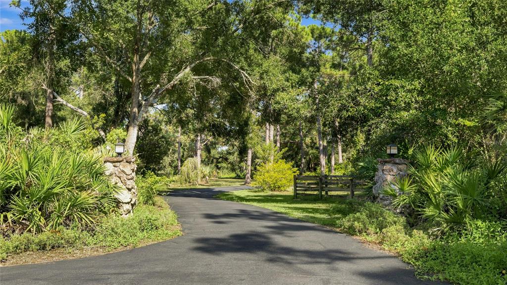 A paved driveway leads through a wooded area past two stone pillars with light fixtures — 6950 EL DORADO DRIVE, SARASOTA, FL