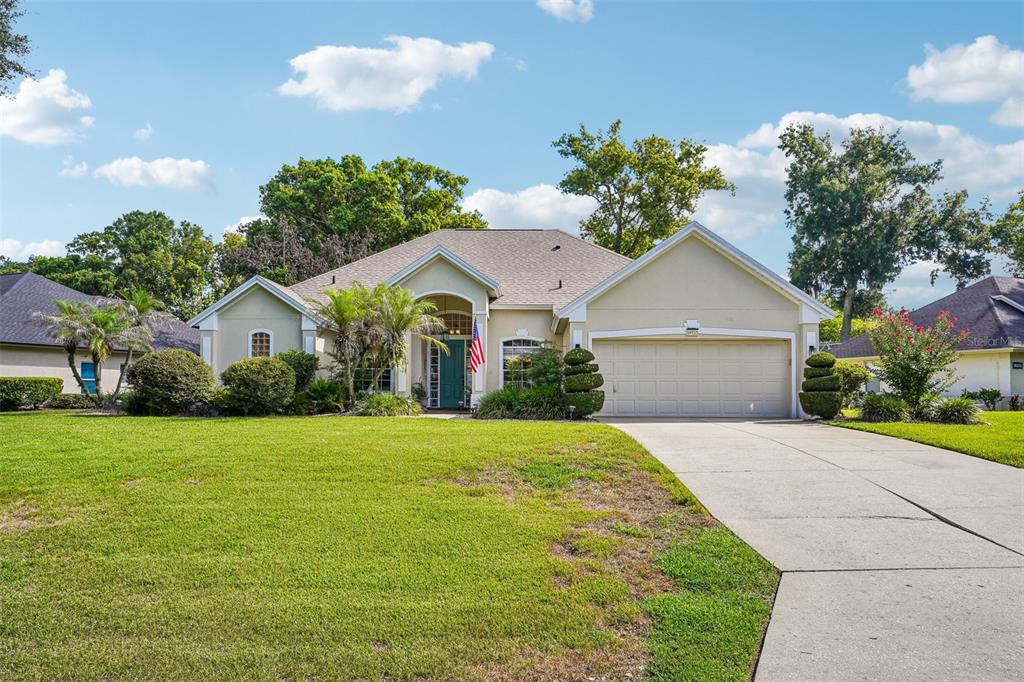 A single-story suburban house with a beige stucco exterior, a two-car garage, and a lawn — 19323 PARK PLACE BOULEVARD, EUSTIS, FL