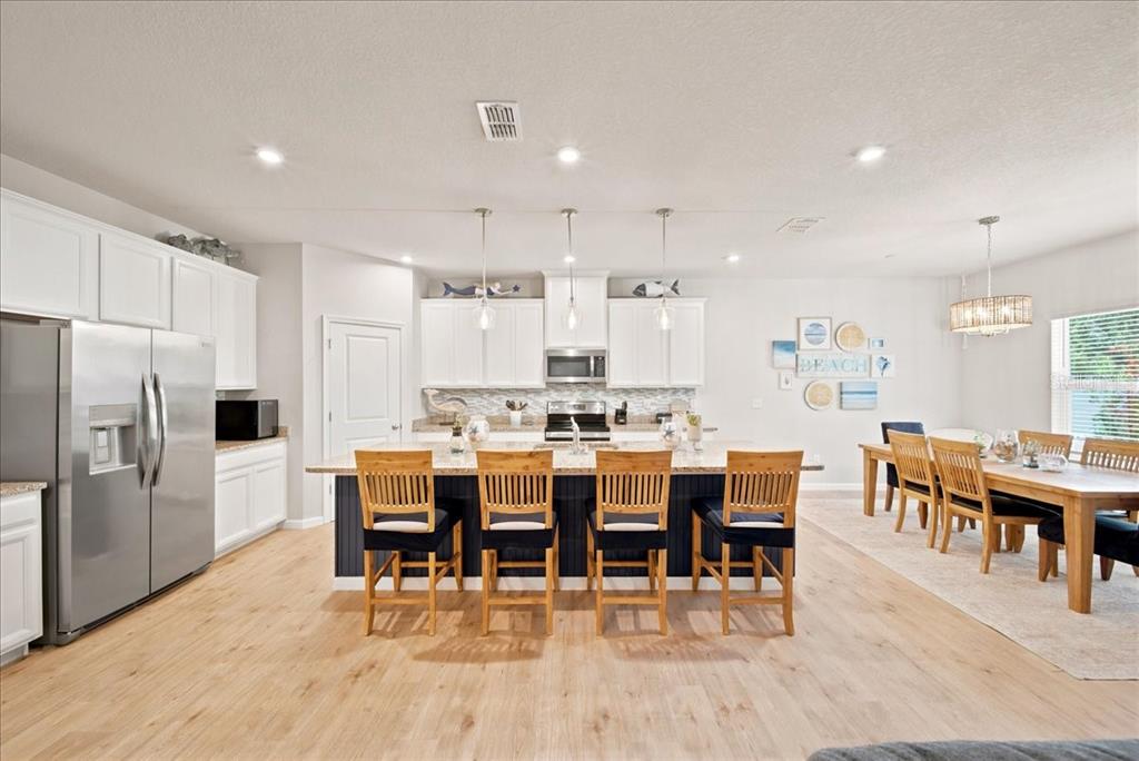 A kitchen with white cabinets, a dark island with four wooden chairs, and a dining area — 11432 64TH STREET E, PARRISH, FL