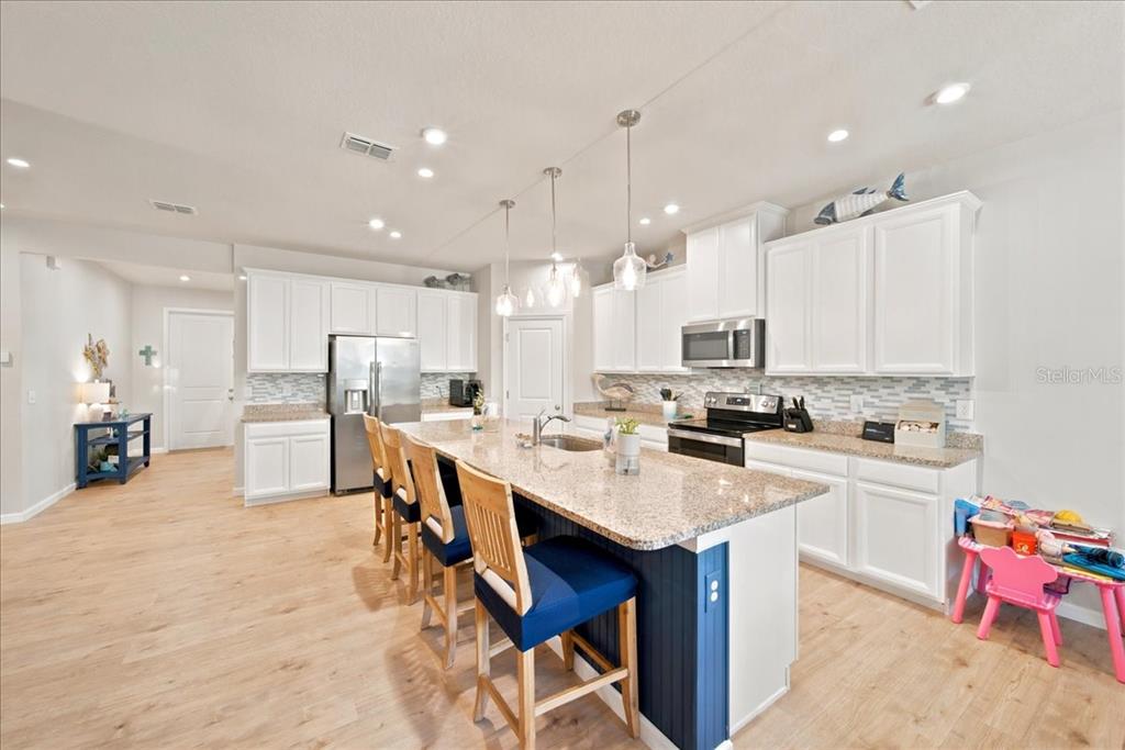 A kitchen features white cabinets, granite countertops, a blue island with seating, and wood flooring — 11432 64TH STREET E, PARRISH, FL