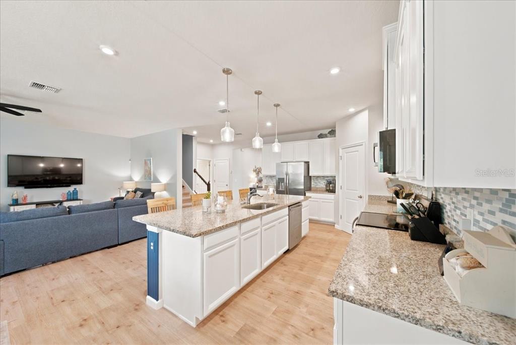 A kitchen with white cabinets, granite countertops, and a central island overlooks a living area — 11432 64TH STREET E, PARRISH, FL