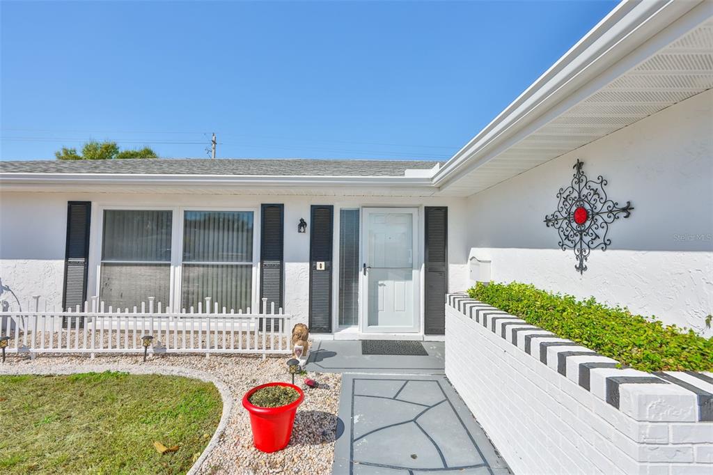 The exterior of a white house features a stone walkway, a red planter, and shutters — 1254 W DEL WEBB BOULEVARD, SUN CITY CENTER, FL