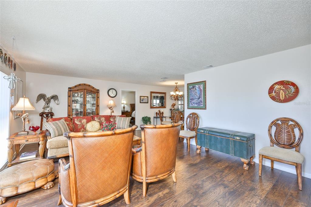 A living room features wood flooring, a floral sofa, two rattan chairs, and vertical blinds — 1254 W DEL WEBB BOULEVARD, SUN CITY CENTER, FL