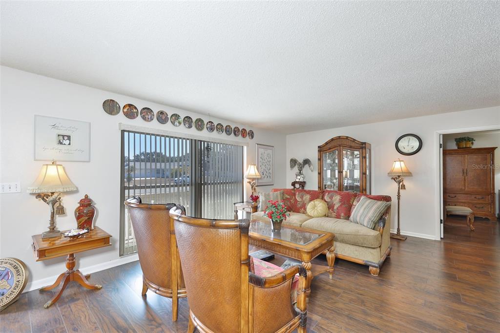 A living room features dark wood flooring, patterned furniture, and a row of decorative wall plates — 1254 W DEL WEBB BOULEVARD, SUN CITY CENTER, FL
