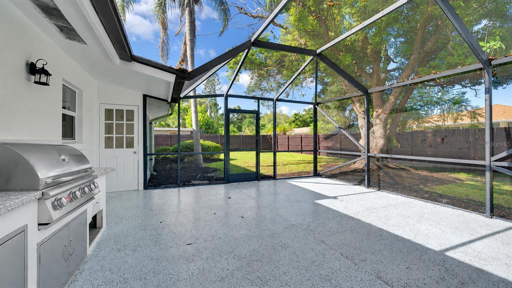 A screened-in patio features a built-in stainless steel grill, light-colored flooring, and a backyard view — 2769 WISTERIA PLACE, SARASOTA, FL