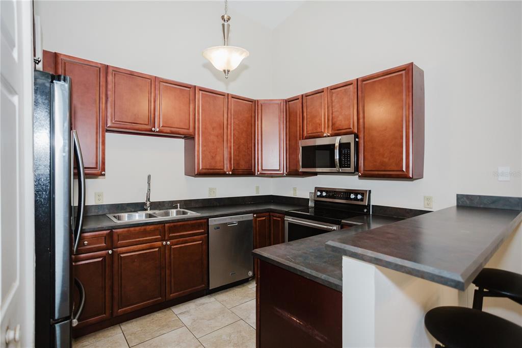 A kitchen features dark wood cabinets, dark countertops, stainless steel appliances, and tile flooring — 3915 NW 7TH PLACE, GAINESVILLE, FL