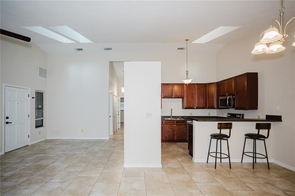 An open-concept kitchen with dark wood cabinets and a breakfast bar overlooks a tiled living area — 3915 NW 7TH PLACE, GAINESVILLE, FL