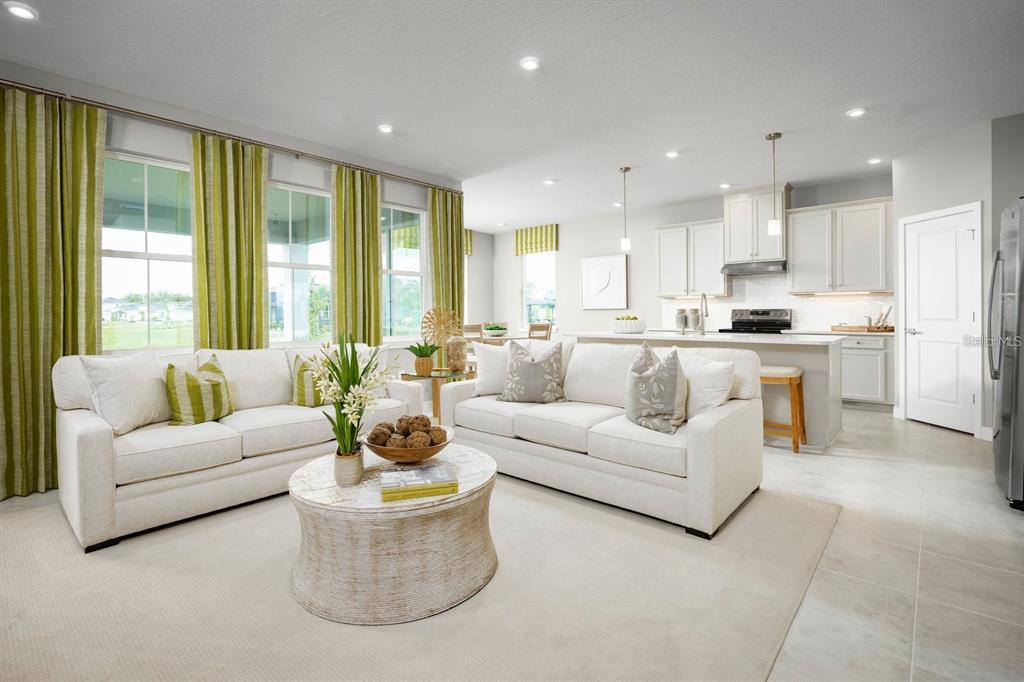 A bright open-concept living room features two white sofas, a round coffee table, and kitchen — 20017 GOLDEN GLOW LOOP, VENICE, FL